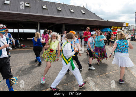 Frauen, die beide von Morris Seiten und Mitglieder der Öffentlichkeit, tanzen die 'gun Dance" mit hölzernen Stäben als Waffen, während auf Broadstairs Harbour Jetty. Stockfoto