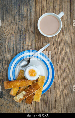 Weich gekochtes Ei, toast, Soldaten und eine Tasse Tee auf Holz von oben Stockfoto