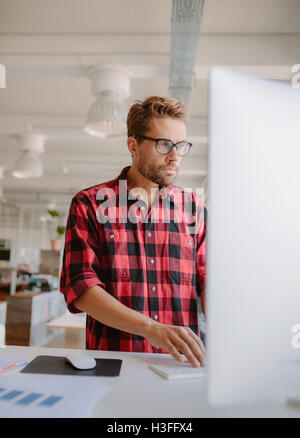 Vertikale Schuss der junge Mann arbeitet am Computer. Geschäftsmann, die Konzentration auf seine Arbeit im modernen Büro. Stockfoto