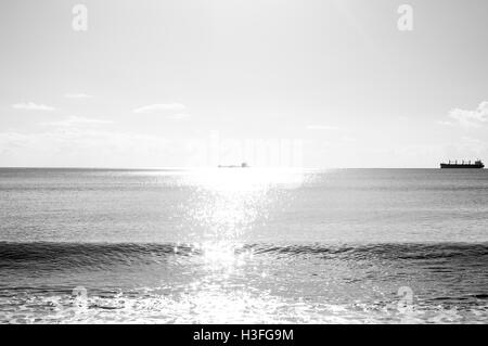 Zwei Frachtschiffe am Horizont, eine in Sonnenlicht getaucht Stockfoto