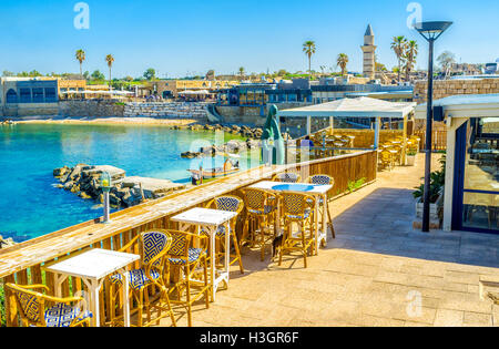 Das outdoor-Restaurant im Hafen von Cäsarea mit Blick auf die Gebäude rund um den Hafen, strahlend blauen Wasser und winzigen Strand Stockfoto