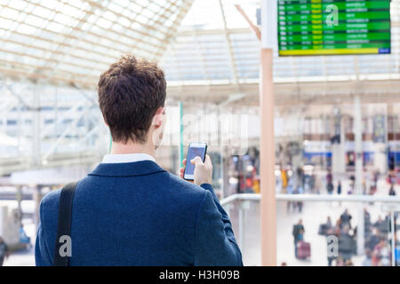Reisende, die SMS auf Smartphone mit Fahrplan im Hintergrund Stockfoto