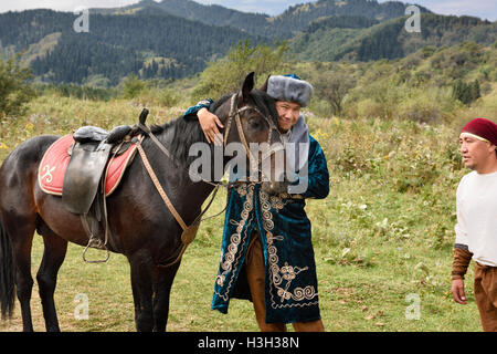 Mann in traditioneller Shapan Mantel und Borik GAP umarmt einen Hengst Hunnen Village Kasachstan Stockfoto