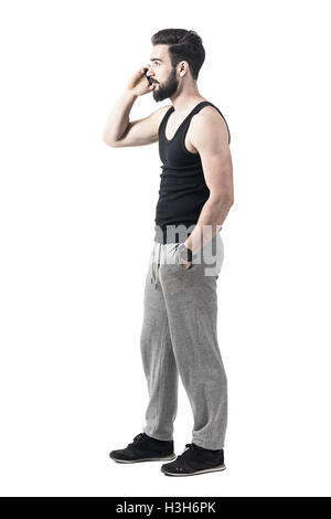 Seitenansicht des jungen Fit muskulöser Mann auf dem Handy, sportliche Kleidung zu tragen. Ganzkörper-Länge-Porträt isoliert auf weiss Stockfoto