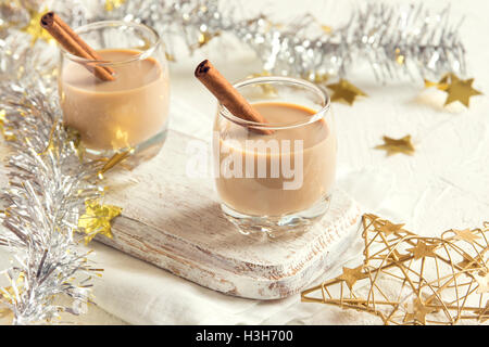Chirstmas Eierlikör mit Zimt im Glas mit goldenen Ornamenten - hausgemachte traditionelle festliche Getränk für die Weihnachtszeit Stockfoto