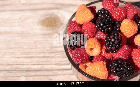 Bio rote und goldene Himbeeren gemischt mit Brombeeren in eine Glasschüssel auf einem rustikalen Bauernhof-Tisch. Stockfoto