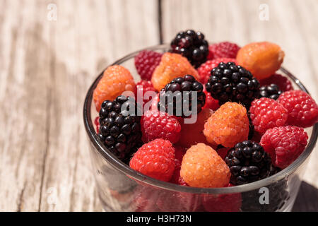 Bio rote und goldene Himbeeren gemischt mit Brombeeren in eine Glasschüssel auf einem rustikalen Bauernhof-Tisch. Stockfoto