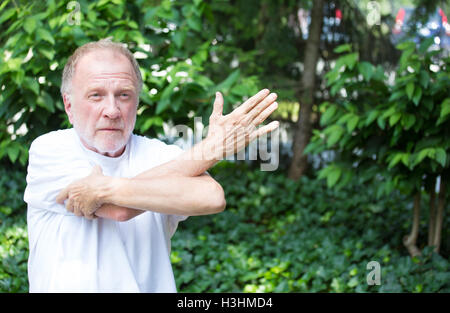 Closeup Portrait, senior reifer Mann im weißen Hemd, streckte Arme, isoliert grünen Bäumen Background. Aufwärmen Stockfoto