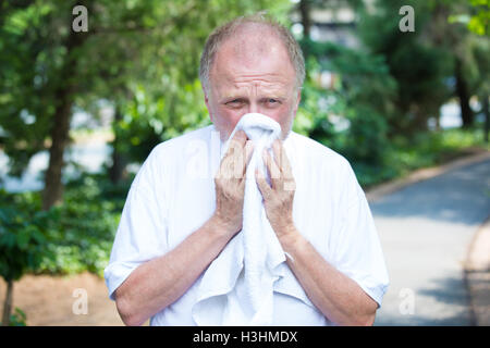 Closeup Portrait, alte Herr im weißen Hemd, Niesen, die Nase Ausblasen, Allergie, leidet an einem heißen sonnigen feuchter Tag Stockfoto