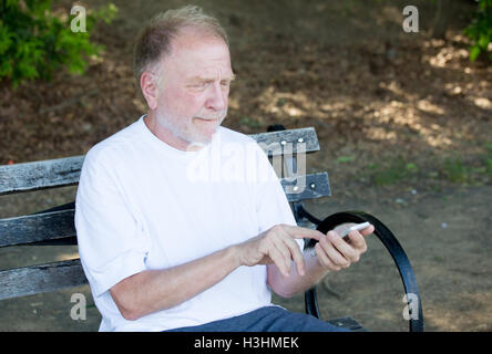 Closeup Portrait von Fett älterer Mann im weißen Hemd, schielen, Überprüfung Smartphone, SMS, sitzend auf einer Bank Stockfoto