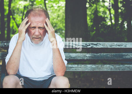 Closeup Portrait, betonte älteren Mann im weißen Hemd, Hände auf den Kopf mit Kopfschmerzen, auf Bank sitzend Stockfoto