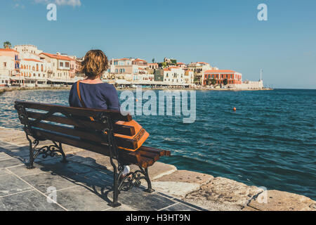 junge Frau auf der Bank sitzen und mit Blick auf den alten Hafen in Chania, Kreta, Griechenland Stockfoto