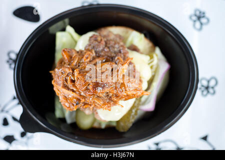 Overhead Schuss einen Burger mit verschiedenen Toppings wie Gurken und zog Schweinefleisch in einem schwarzen Kunststoff-Lebensmittel-Behälter Stockfoto