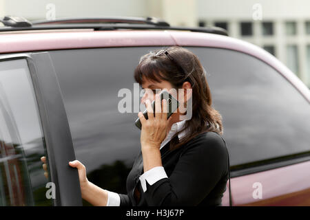 Reife Frau am Handy hält die Autotür öffnen geben Sie Stockfoto