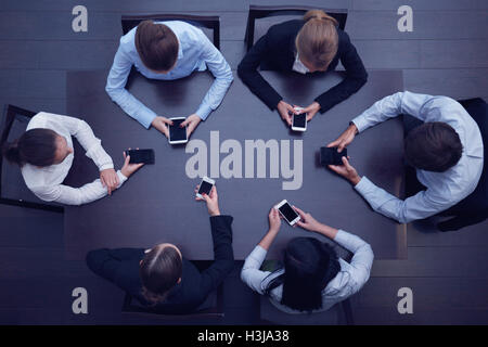 Geschäftsleute mit Smartphones sitzen um den Tisch, Ansicht von oben Stockfoto