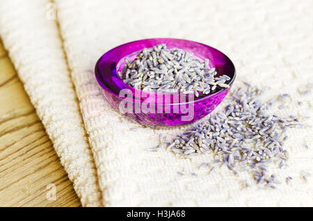 Getrocknete Lavendelblüten in lila Glasschüssel auf Stoff und Holz. Lavandula Angustifolia mit blassen lila Blüten. Küchenkraut. Stockfoto