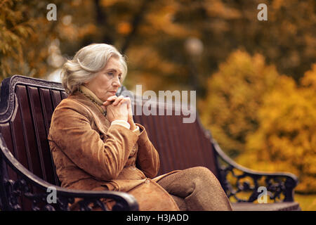 Traurig ältere Frau sitzen auf einer Bank im Herbst park Stockfoto