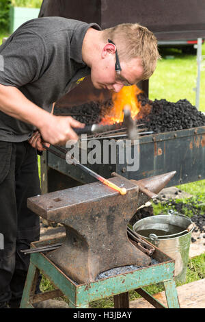 Ein Schmied ist rot Roheisen auf einem Amboss vor einer Schmiede hämmern. Stockfoto