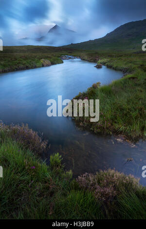 Nant Gwryd fließt von Llyn Cwmffynnon in den kühlen blauen Dämmerlicht. Crib Goch und der Snowdon Horseshoe ist in Wolken gehüllt Stockfoto