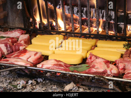 viel rohes Rindfleisch und Schweinefleisch kochen im Kamin mit einem warmen Feuer und gelbe polenta Stockfoto