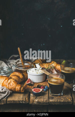 Frühstück mit Croissants, Ricotta-Käse, Feigen, frische Beeren, Schinken, Fleisch, Honig und Espresso-Kaffeemaschine auf rustikalen hölzernen tabl Stockfoto