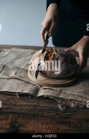 Frau frisch gebackenes Roggenbrot auf einem rustikalen Holztisch schneiden Stockfoto