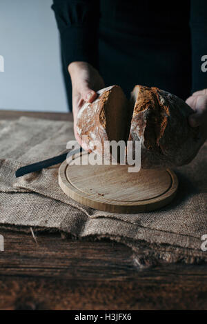 Frau frisch gebackenes Roggenbrot auf einem rustikalen Holztisch schneiden Stockfoto