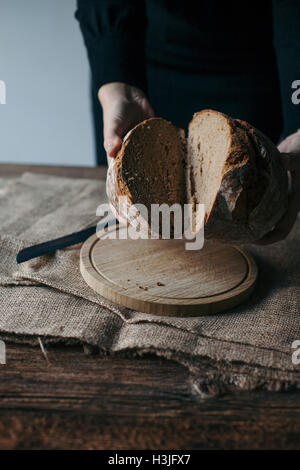 Frau frisch gebackenes Roggenbrot auf einem rustikalen Holztisch schneiden Stockfoto