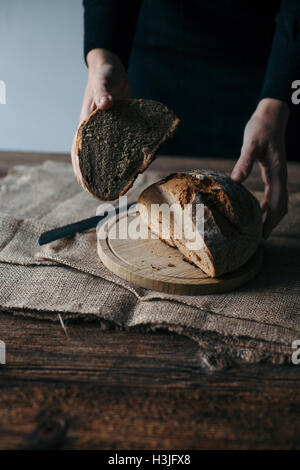 Frau frisch gebackenes Roggenbrot auf einem rustikalen Holztisch schneiden Stockfoto