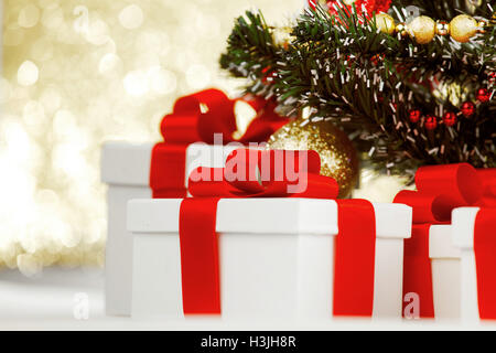 Studioaufnahme von weißen Geschenken mit roten Bändern unter Weihnachtsbaum auf Bokeh Hintergrund Stockfoto