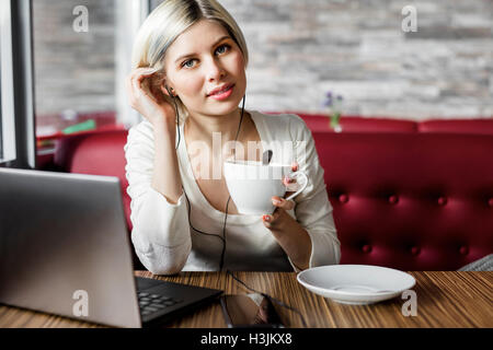 Junge Frau mit Kaffeetasse und Laptop im Cafe Stockfoto