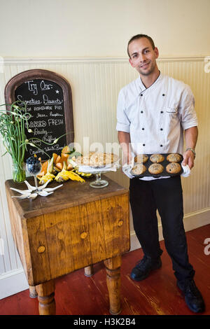 Küchenchef mit frischen Muffins und Kuchen auf Anzeigetabelle Stockfoto