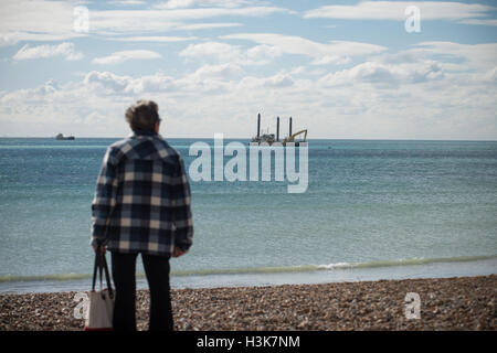 Eine Frau steht am Strand in Lancing West Sussex, England und sieht eine große Bau-Schiff auf der Baustelle für die neue Rapunzeln Offshore-Windpark. Bau der Windfarm durch den Energiekonzern EON wird voraussichtlich im Jahr 2018 abgeschlossen sein. Stockfoto