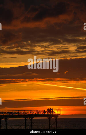 Aberystwyth, Wales, UK. 9. Oktober 2016. UK-Wetter: Red Sky at Night - am Ende eines Tages fast ununterbrochenen Sonnenschein an der Westküste von Wales, eine Gruppe von Menschen stehen am Ende Aberystwyths Meer Pier, genießen Sie das Spektakel eines spektakulären Sonnenuntergangs über Cardigan Bay Photo Credit: Keith Morris/Alamy Live News Stockfoto