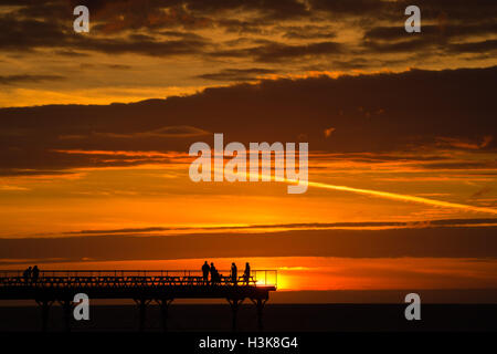 Aberystwyth, Wales, UK. 9. Oktober 2016. UK-Wetter: Red Sky at Night - am Ende eines Tages fast ununterbrochenen Sonnenschein an der Westküste von Wales, eine Gruppe von Menschen stehen am Ende Aberystwyths Meer Pier, genießen Sie das Spektakel eines spektakulären Sonnenuntergangs über Cardigan Bay Photo Credit: Keith Morris/Alamy Live News Stockfoto