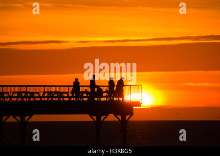 Aberystwyth, Wales, UK. 9. Oktober 2016. UK-Wetter: Red Sky at Night - am Ende eines Tages fast ununterbrochenen Sonnenschein an der Westküste von Wales, eine Gruppe von Menschen stehen am Ende Aberystwyths Meer Pier, genießen Sie das Spektakel eines spektakulären Sonnenuntergangs über Cardigan Bay Photo Credit: Keith Morris/Alamy Live News Stockfoto