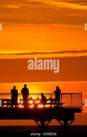 Aberystwyth, Wales, UK. 9. Oktober 2016. UK-Wetter: Red Sky at Night - am Ende eines Tages fast ununterbrochenen Sonnenschein an der Westküste von Wales, eine Gruppe von Menschen stehen am Ende Aberystwyths Meer Pier, genießen Sie das Spektakel eines spektakulären Sonnenuntergangs über Cardigan Bay Photo Credit: Keith Morris/Alamy Live News Stockfoto