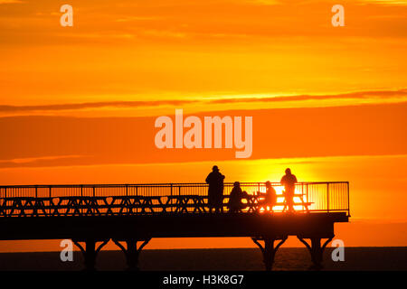 Aberystwyth, Wales, UK. 9. Oktober 2016. UK-Wetter: Red Sky at Night - am Ende eines Tages fast ununterbrochenen Sonnenschein an der Westküste von Wales, eine Gruppe von Menschen stehen am Ende Aberystwyths Meer Pier, genießen Sie das Spektakel eines spektakulären Sonnenuntergangs über Cardigan Bay Photo Credit: Keith Morris/Alamy Live News Stockfoto