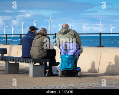 Zwei Männer und eine Frau sitzen auf der Redcar-Promenade, Blick auf das Meer an einem kühlen Herbsttag. Stockfoto