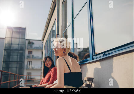 Drei junge Frauen sitzen auf Balkon an einem sonnigen Tag. Freundinnen genießen freie Zeit zusammen im Freien. Stockfoto