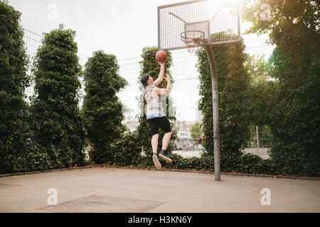 Junger Mann springen und Dunks Basketball in Reifen. Teenager Kerl spielt Streetball. Stockfoto