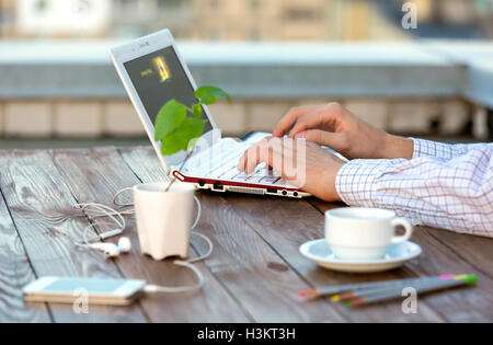 Person Tippen auf Laptop-Computer am Schreibtisch aus Holz mit Blume Stockfoto