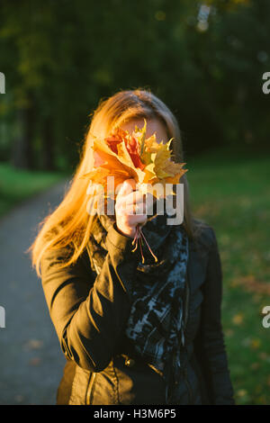 Junge Frau Gesicht hinter Haufen im Herbst Laub versteckt Stockfoto