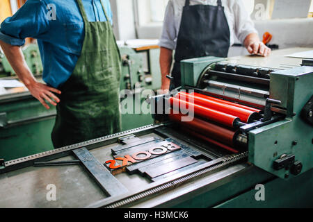 Senior-Handwerker/Techniker Betreuung jungen Mann auf Letterpress Maschine in Buch-Kunst-Werkstatt, Mittelteil Stockfoto