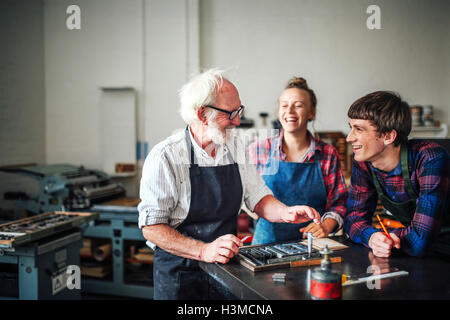 Senior Handwerker Lachen mit junge Handwerker und Handwerkerin in Buchdruck-Werkstatt Stockfoto