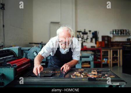 Senior Handwerker bücken und mit Holzbuchstaben und Letterpress Maschine in Buch-Kunst-Werkstatt Stockfoto