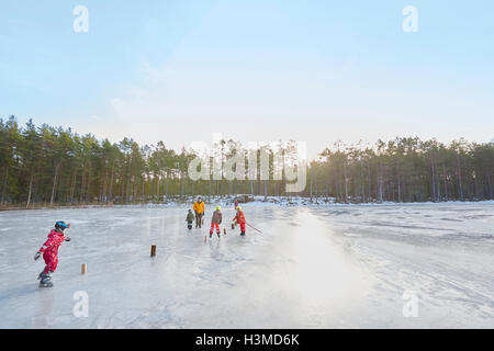 Älteres Paar und Enkel üben Eislaufen Slalom am zugefrorenen See, Hotels, Schweden Stockfoto