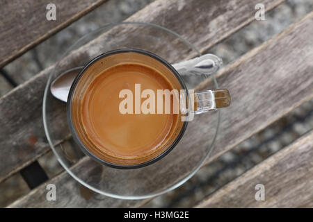 Türkische frisch gebraut natürlicher gemahlener Kaffee mit Milch in transparentem Glastasse mit Untertasse über Vintage Holztisch, Detail-cl Stockfoto