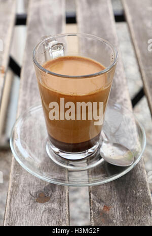 Türkische frisch gebraut natürlicher gemahlener Kaffee mit Milch in transparenten Ganzglas-Tasse mit Untertasse über Vintage Holztisch, clos Stockfoto