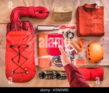 Draufsicht des Mannes Hand, die erste-Hilfe-Kit über Kletterausrüstung mit Helm, Rucksack und Kletterseilen verpackt Stockfoto
